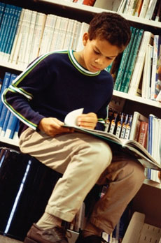 Foto de um menino lendo numa biblioteca