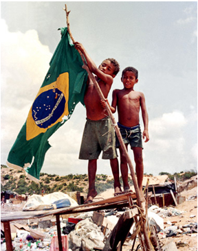 Dois-meninos-sem-camisa-em-meio-a-um-ambiente-cheio-de-lixo-erguendo-uma-bandeira-rasgada-do-Brasil