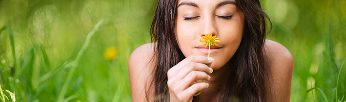 mulher de olhos fechados cheirando uma flor