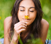 mulher de olhos fechados cheirando uma flor