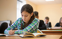 aluna sentada na sala de aula estudando com livro e escrevendo no caderno